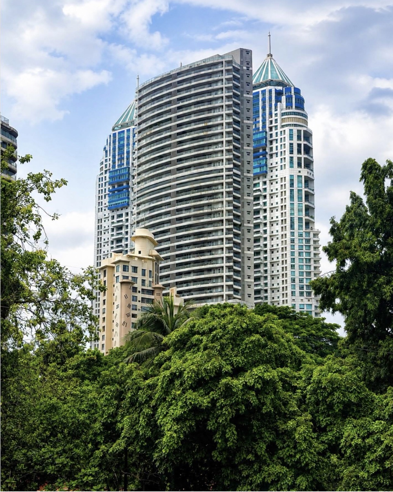 Residential towers framed by green trees beneath a blue sky